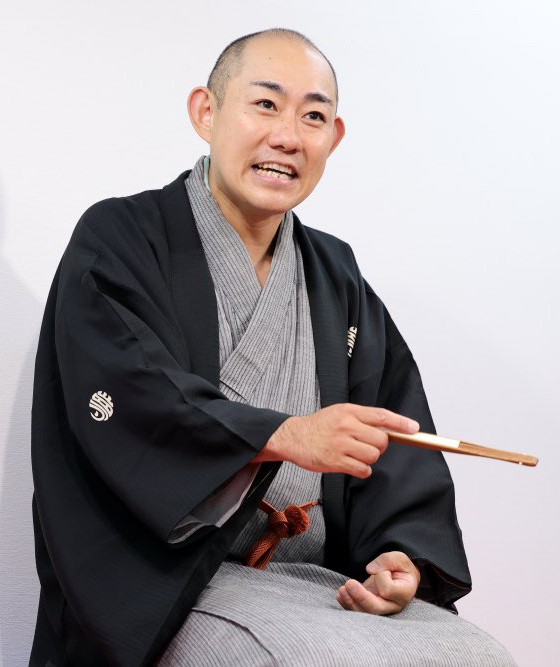 三笑亭夢丸（さんしょうてい ゆめまる）師匠が、黒い羽織を着て、扇子を手にしている写真